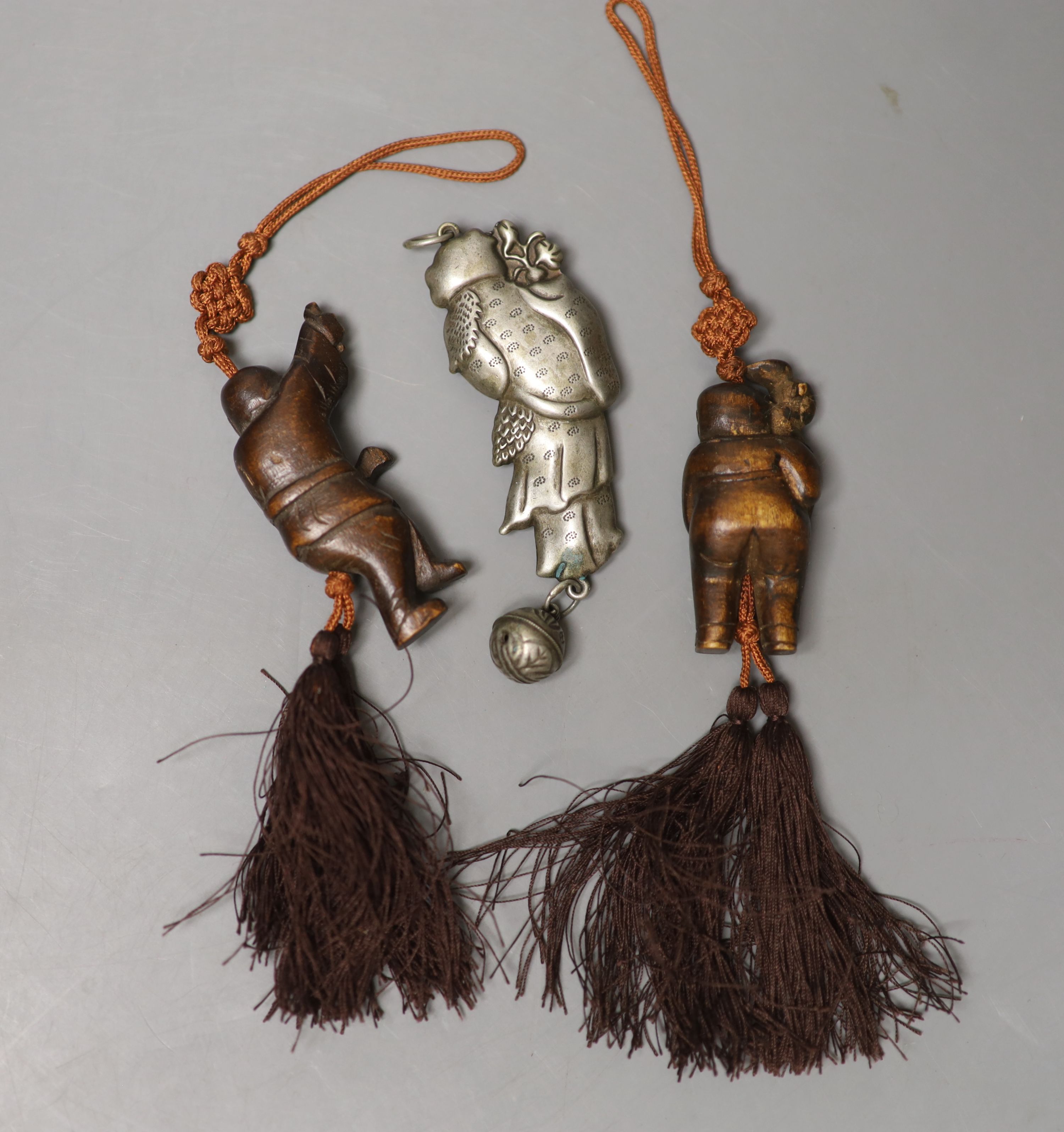 A Chinese metal baby's rattle and two carved wood figural pendants